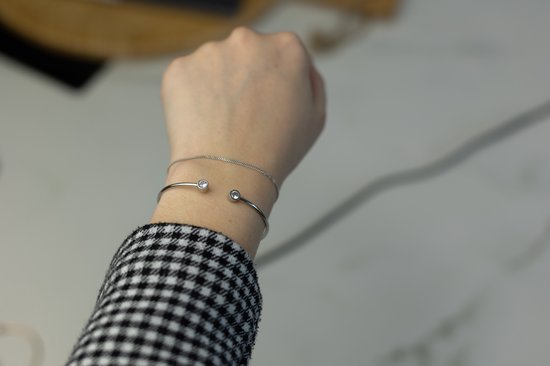 Gouden armband met een subtiel zilverkleurig kettinkje, versierd met twee ronde kristallen, gedragen op een met ruitjespatroon beklede arm.