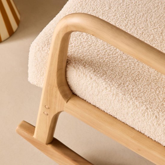 Detail van een schommelstoel met een licht houten armleuning en crèmekleurige bouclé bekleding.