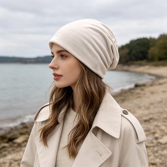 Vrouw met een crème beanie, kijkend naar de zee.
