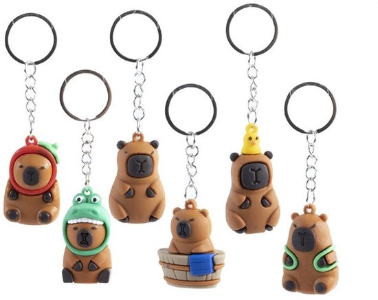 Zeven bruine capybara sleutelhangers met verschillende accessoires, waaronder een kikkerhelm en een badkuip.
