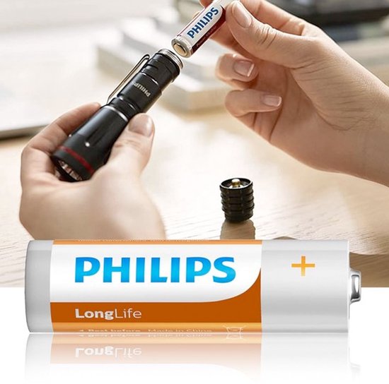 Mains insérant une pile AA Philips LongLife dans une lampe torche noire. Gros plan d'une pile avec étiquette orange et blanche.