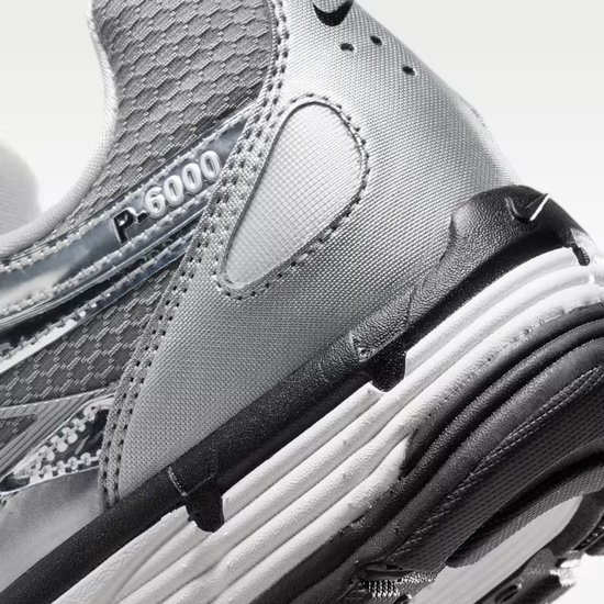 Close-up van de achterkant en zijkant van de grijze Nike P-6000 sneaker. Zwarte zool met witte lagen en 'P-6000' op de zijkant.