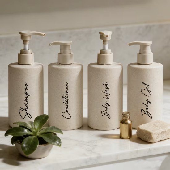 Vier beige zeepdispensers met pompsysteem, gemarkeerd met 'Shampoo', 'Conditioner', 'Body Wash' en 'Body Gel'. Een kleine plant en stuk zeep staan ernaast.