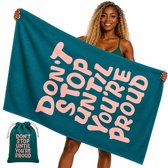 Groene strandhanddoek met de tekst 'DON'T STOP UNTIL YOU'RE PROUD' in roze letters, vastgehouden door een vrouw.