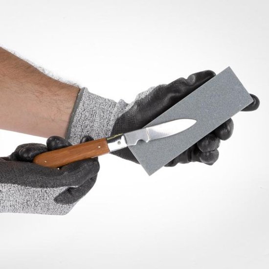Handen met werkhandschoenen die een zakmes slijpen op een grijze Kreator slijpsteen.