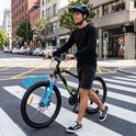 Man loopt met een zwarte TIGER MTB-fiets met blauwe voorvork over een zebra.