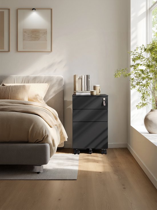 Zwarte archiefkast met 3 lades, naast een bed, met boeken en een mok op het bovenste blad.