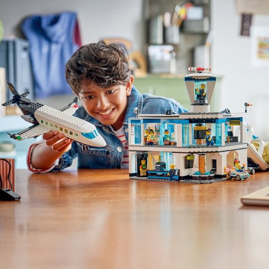 Jongen houdt een LEGO City vliegtuig vast voor een LEGO City luchthaven met toren en passagiers.