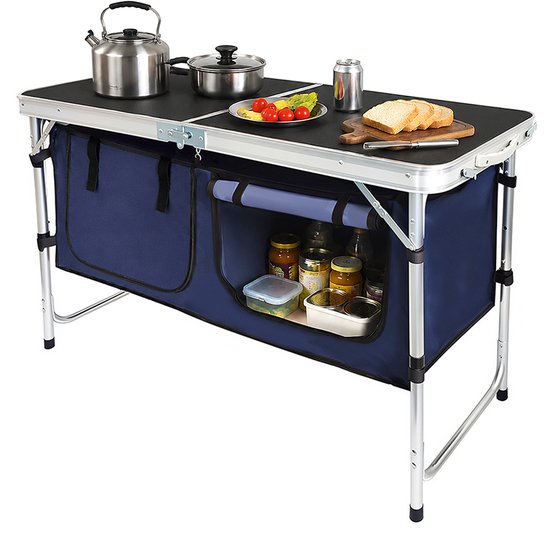 Opvouwbare campingtafel met donkerblauwe opbergvakken, gevuld met potten en voedsel, met een waterkoker, pan en brood op het tafelblad.