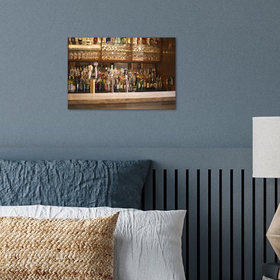 Poster met flessen drank en glazen op een bar, boven een bed met blauwe kussens.