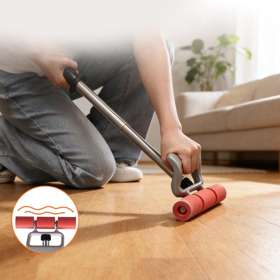 Een persoon rolt met een grijze rol met rode wielen over een houten vloer in een woonkamer.