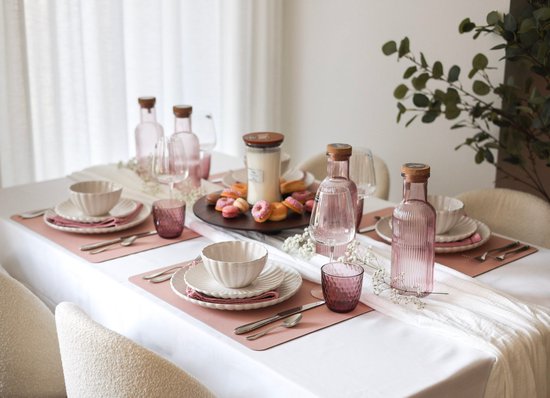 Table dressée avec des verres à eau roses, des assiettes blanches, des sets de table roses et des donuts.