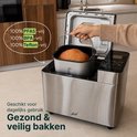Hand haalt een brood uit een zilverkleurige broodbakmachine.