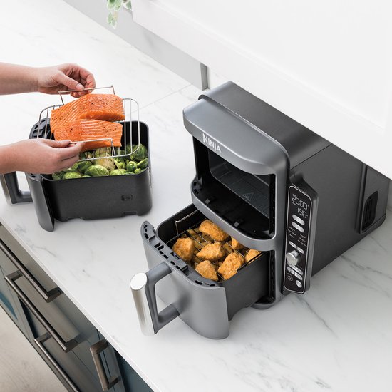 Een grijze Ninja Double Stack Airfryer XXL met de laden open. Eén lade bevat kipnuggets, de andere lade wordt gevuld met zalm en spruitjes.