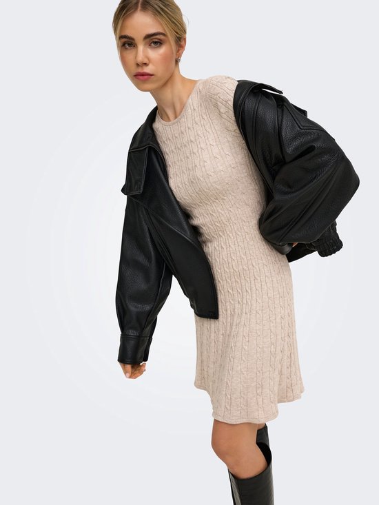 Model draagt een beige gebreide jurk met kabels en zwarte leren jack.