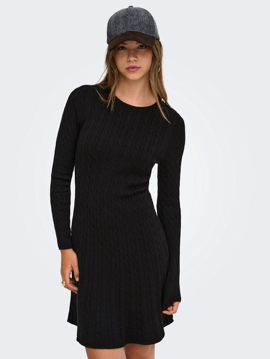 Model in een zwarte gebreide mini-jurk met kabels en lange mouwen, met een pet.