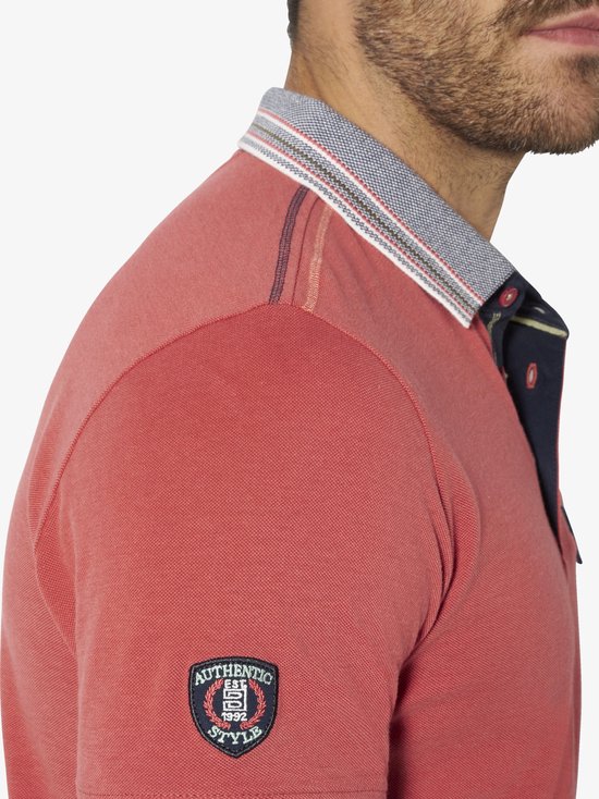 Detailopname van de schouder van een lichtrood poloshirt met een 'Authentic Style' embleem op de mouw.
