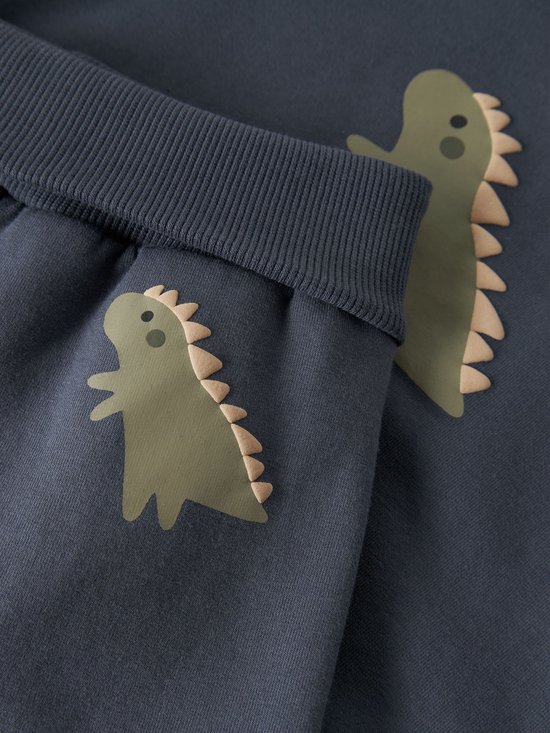 Detail van een dino-opdruk op een donkerblauwe broek.