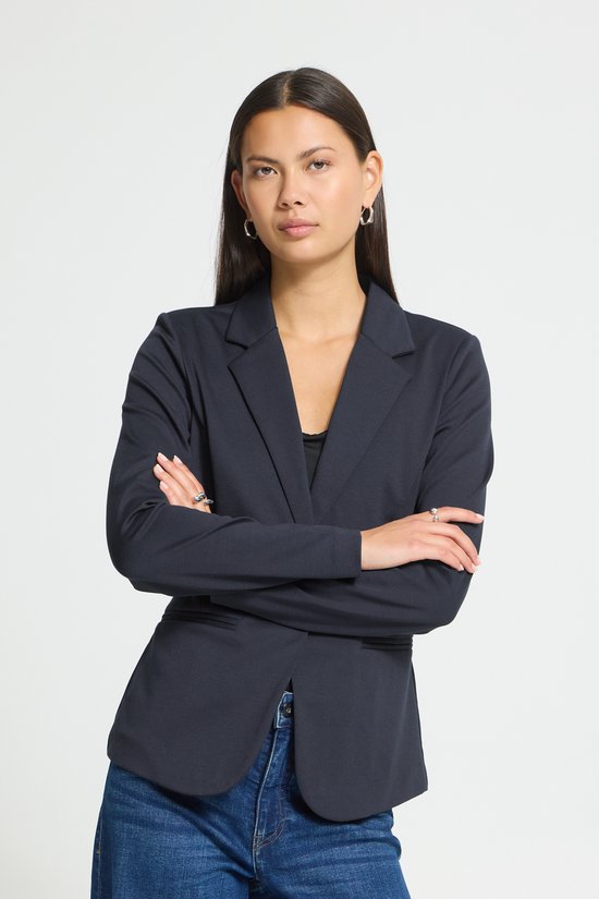 Donkerblauwe blazer met lange mouwen, gedragen door een model met armen over elkaar.