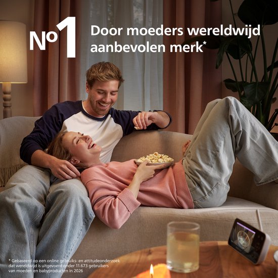 Ouders ontspannen op de bank met popcorn terwijl de babyfoon op tafel het kind in de kamer toont.