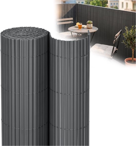 Donkergrijs PVC-scherm opgerold, met verticale lamellen. Op de achtergrond een balkon met tafel en stoelen.