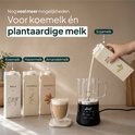 Zwarte melkopschuimer met glazen kan, terwijl sojamelk in de kan wordt gegoten, naast pakken melk, havermelk en amandelmelk.