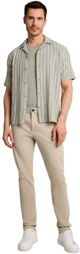 Model draagt een beige slim-fit chino broek, een olijfgroen shirt en een gestreept overhemd met witte sneakers.