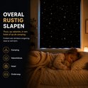 Meisje slaapt op bed naast een raam met een zwart sterren gordijn, ideaal voor rustige slaap.