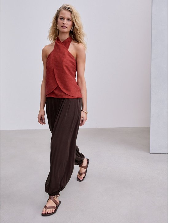 Model loopt in een bruine ballonbroek, roodbruine top en bruine sandalen.