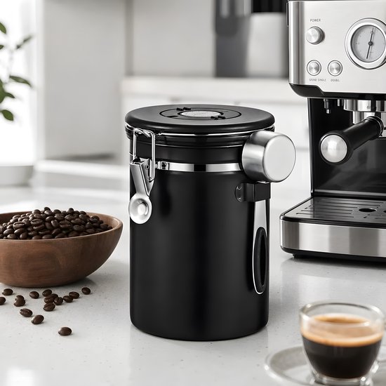 Zwarte RVS koffiebewaarpot in een keukenomgeving, naast een espressomachine, een kom koffiebonen en een kopje espresso.