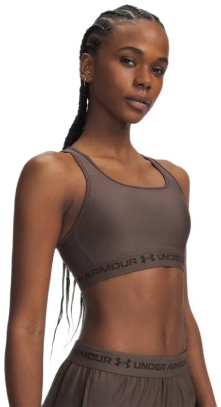 Model met bruine Under Armour sportbeha met gekruiste bandjes en logo, haar in vlechten.