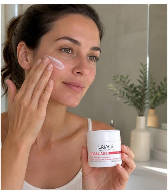 Model brengt Uriage Roséliane rijke crème aan op haar wang. Potje met crème is zichtbaar.