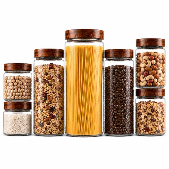 Ensemble de sept bocaux en verre avec couvercles en bois, remplis de pois chiches, riz, muesli, spaghettis, grains de café, noix et muesli.