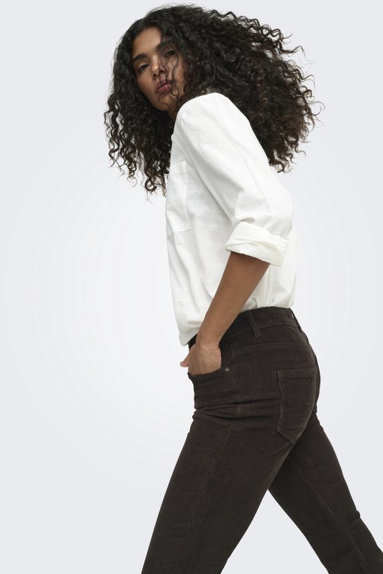 Model met krullend haar draagt een bruine corduroy flared broek met witte blouse.