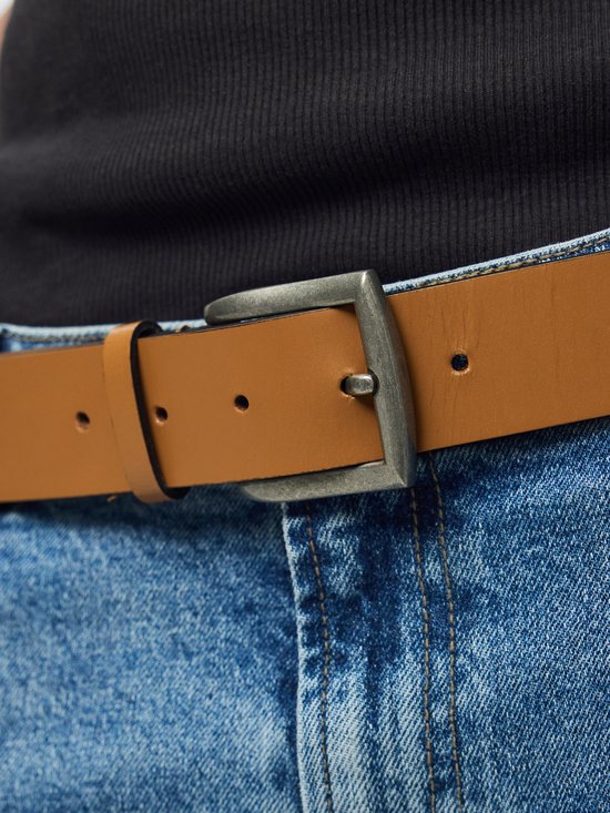 Bruine leren riem met een metalen gesp, gedragen op een spijkerbroek.