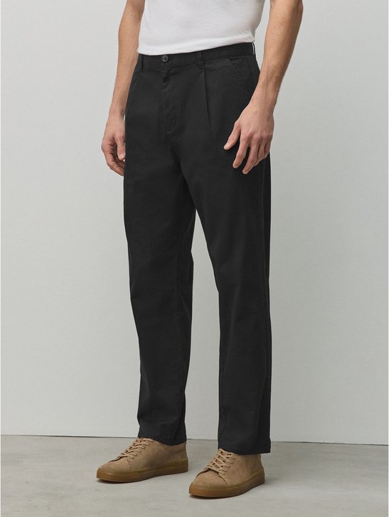 Model draagt een zwarte chino met taps toelopende pijpen, gecombineerd met beige suède schoenen.
