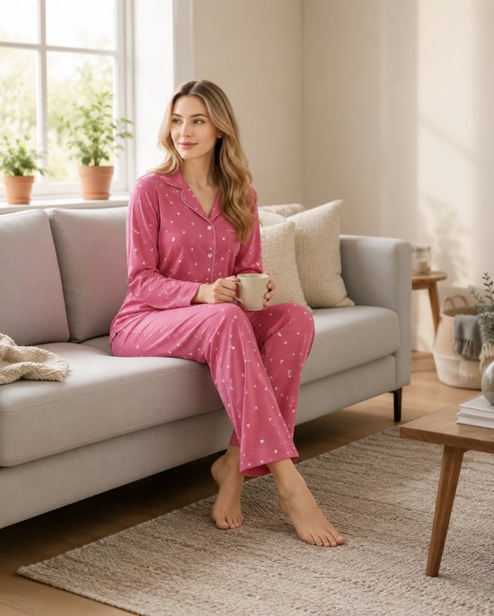 Vrouw in roze pyjama met hartjesprint, zittend op een bank met een mok.