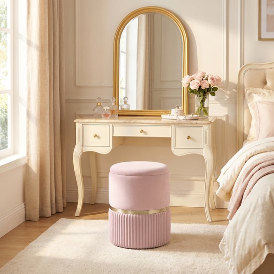Roze fluwelen poef met opbergruimte in een slaapkamer bij een kaptafel.