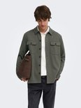 Man met donkerbruine tas, draagt een olijfgroene utility blouse over een wit poloshirt.