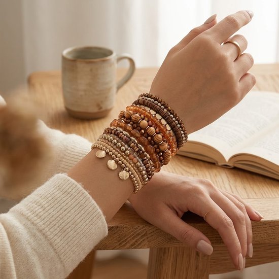 Een vrouw draagt een set van 18 bruine, beige en goudkleurige armbanden met kralen en schelpbedels.