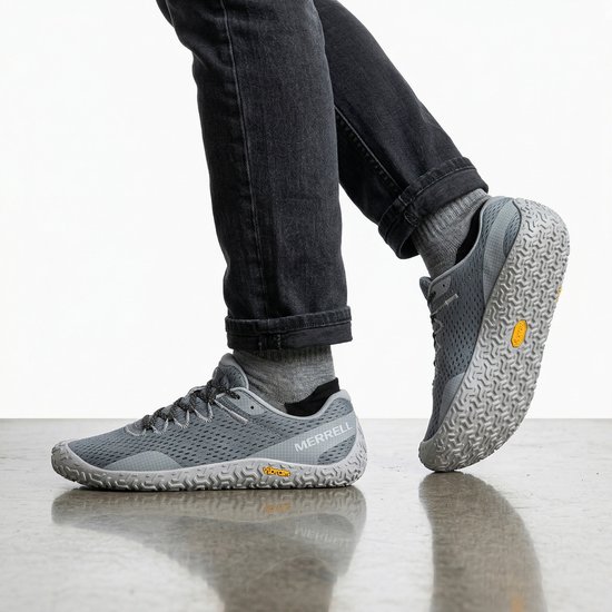Persoon die grijze Merrell Vapor Glove 6 schoenen draagt, met jeans en grijze sokken.