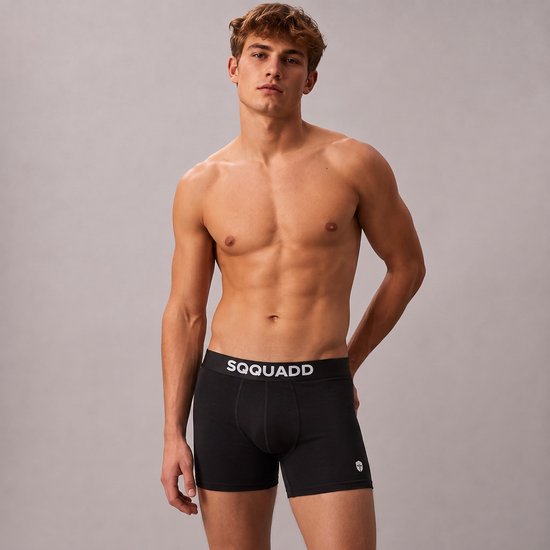 Man met gespierd lichaam draagt een zwarte SQQUADD boxershort met witte band en logo.