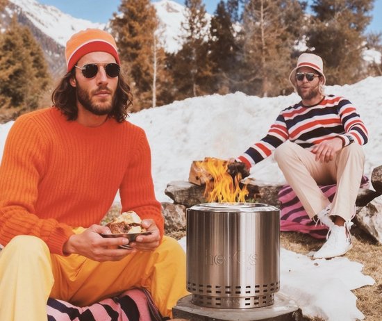 Twee mannen zitten in een besneeuwd landschap bij een brandende herQs vuurkorf.