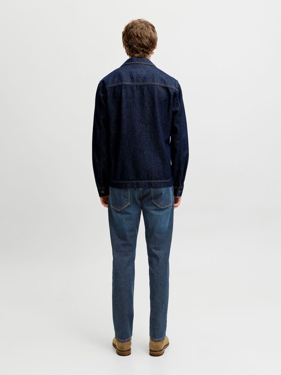 Achteraanzicht van een model in een donkerblauw denimjack en een medium blauwe jeans.