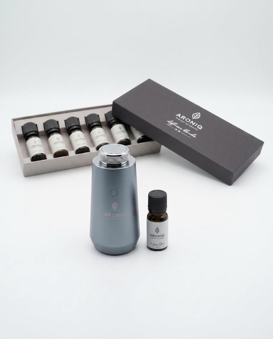 Grijze aroma diffuser, naast een open doos met 6 flesjes etherische olie en een flesje 'Signature Herbs'. Giftset, geschikt voor aromatherapie.