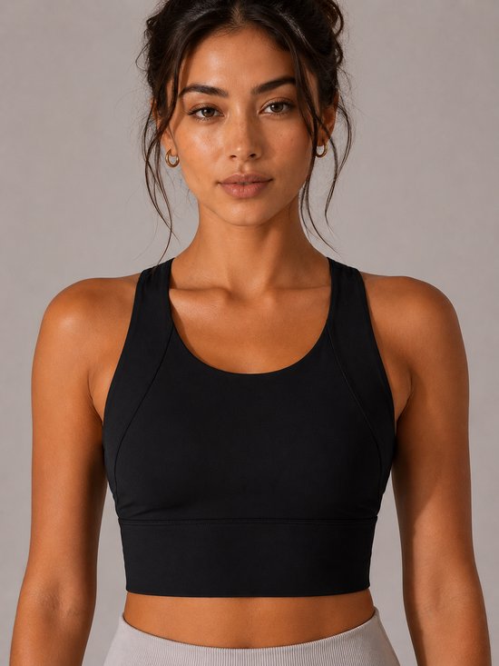 Model draagt zwarte sportbeha met racerback. De beha heeft een brede band aan de onderkant en naden op de cups.