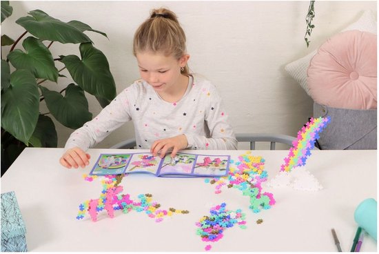 Meisje bouwt met Plus-Plus blokjes aan eenhoorns en regenboog, instructieboekje ernaast.