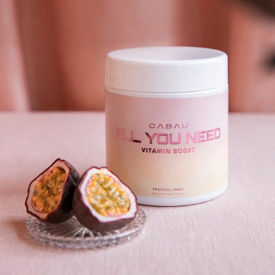 Cabau "All You Need Vitamin Boost" pot met roze en gele gradiënt, naast twee passievruchten op een roze ondergrond.