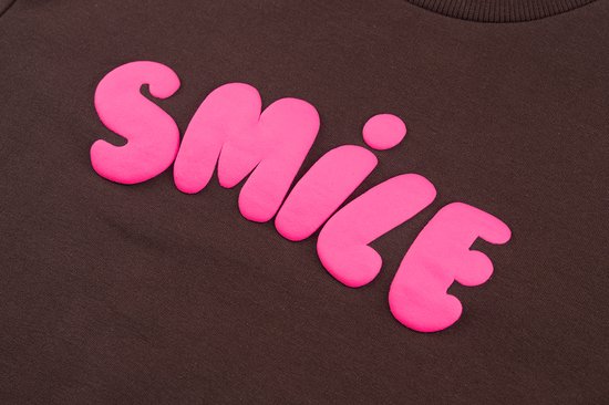 Bruine sweater met felroze, bobbelige letters die "SMILE" spellen.