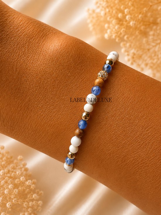 Armband met witte, bruine en blauwe kralen en gouden accenten, gedragen op een arm.